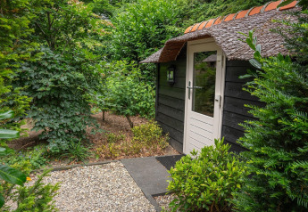 Entrance to a charming lodge with a thatched roof, surrounded by lush green plants in the Netherlands.