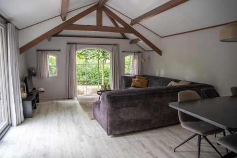 Woonkamer van Heivlinder Comfort 4+2p lodge in Nederland met grote ramen, balken en grijze zetel.