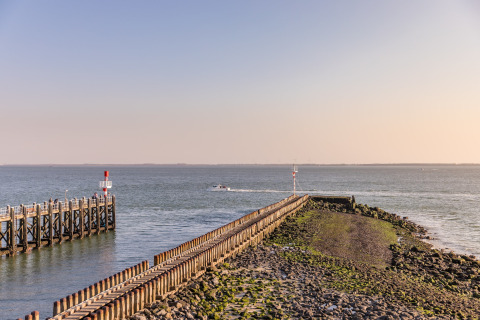 View of a long pier extending into the sea from the beach, with calm water and a boat in the distance.