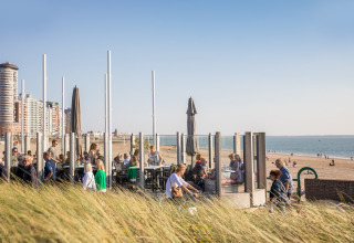 Menschen entspannen sich auf der Terrasse eines Strandhauses mit Blick auf das Meer und die Stadt.
