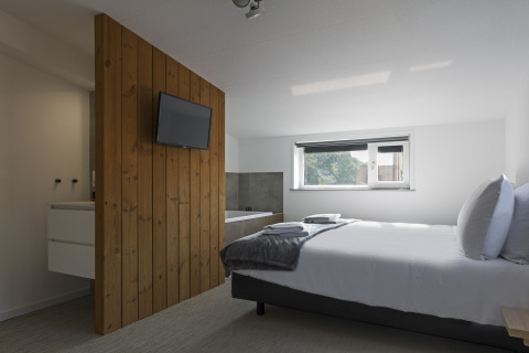 Modern bedroom at Noordzee Resort Vlissingen 3 with double bed, wall-mounted TV, wood panel, and window.