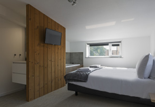 Modern bedroom at Noordzee Resort Vlissingen 3 with double bed, wall-mounted TV, wood panel, and window.
