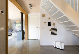 Bright modern entryway with staircase, wall hooks, bags, and a view into the living room at Noordzee Resort Vlissingen.