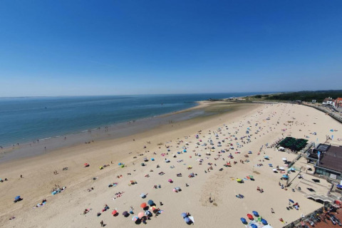 Blick vom Strandhaus auf einen belebten Sandstrand mit bunten Sonnenschirmen und ruhigem Meer.