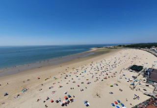 Blick vom Strandhaus auf einen belebten Sandstrand mit bunten Sonnenschirmen und ruhigem Meer.