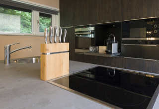 Modern kitchen at Noordzee Resort Vlissingen 3 with glass cooktop, knife block, coffee maker and window view.