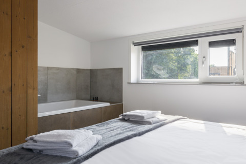 Bright bedroom with a bathtub, large window, and neatly folded towels at Noordzee Resort Vlissingen beach house.