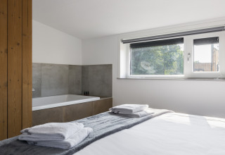 Bright bedroom with a bathtub, large window, and neatly folded towels at Noordzee Resort Vlissingen beach house.