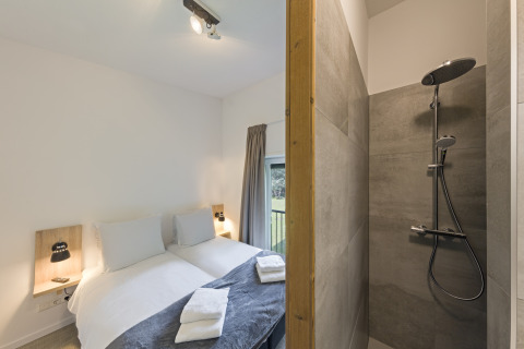 Modern bedroom with twin beds and adjacent walk-in shower at Noordzee Resort Vlissingen 3 in the Netherlands.