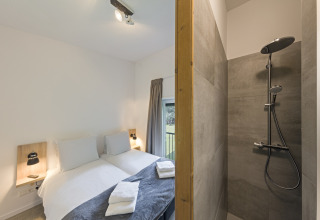Modern bedroom with twin beds and adjacent walk-in shower at Noordzee Resort Vlissingen 3 in the Netherlands.