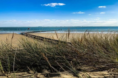Strandlandschaft mit Dünen und Meer, blauer Himmel und vereinzelte Wolken, gesehen vom Strandhaus.