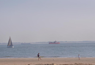 Zwei Personen spielen am Strand Fußball, im Hintergrund sind Segel- und Frachtschiffe auf dem Meer zu sehen.