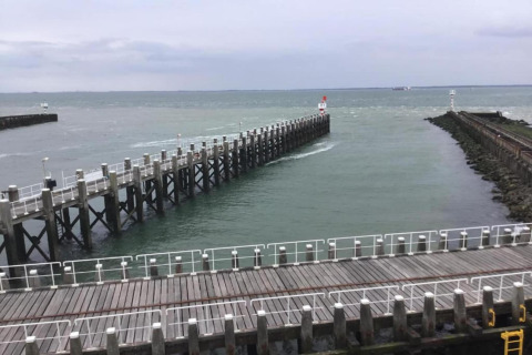 Blick von einem Strandhaus auf einen langen Pier, der ins Meer ragt, umgeben von Leitplanken.
