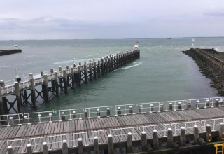 Blick von einem Strandhaus auf einen langen Pier, der ins Meer ragt, umgeben von Leitplanken.