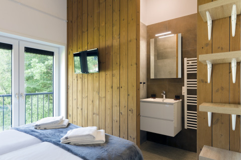 Modern bedroom with en-suite bathroom, wooden accents, TV, and large window at Resort Vlissingen 3, Netherlands.