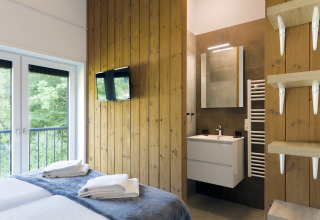 Modern bedroom with en-suite bathroom, wooden accents, TV, and large window at Resort Vlissingen 3, Netherlands.