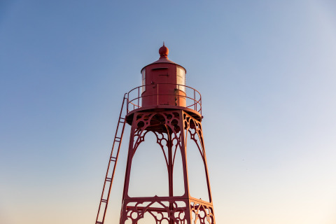 Red iron lighthouse with ladder at Noordzee Resort Vlissingen beach house in the Netherlands, clear sky.