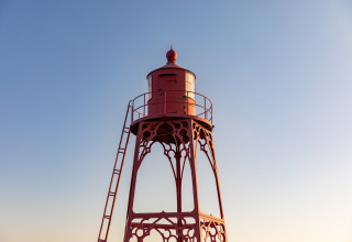 Red iron lighthouse with ladder at Noordzee Resort Vlissingen beach house in the Netherlands, clear sky.