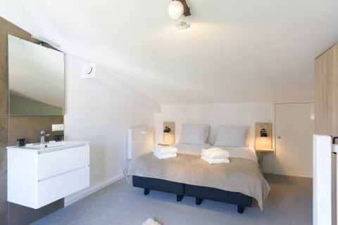 Helles Schlafzimmer mit Doppelbett und Waschbecken im Strandhaus Noordzee Resort Vlissingen 2, Niederlande.