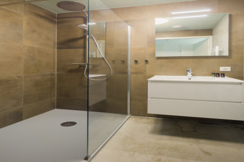 Modernes Bad mit Glasdusche, weißem Waschbecken und Spiegel im Strandhaus «Noordzee» Resort Vlissingen 2, Niederlande.