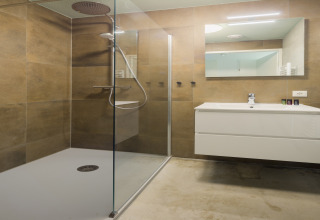 Modernes Bad mit Glasdusche, weißem Waschbecken und Spiegel im Strandhaus «Noordzee» Resort Vlissingen 2, Niederlande.