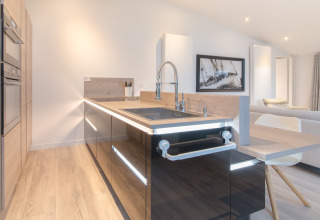 Cucina moderna lodge con mobili neri lucidi, dettagli in legno e isola al Water Resort Oosterschelde, Paesi Bassi.