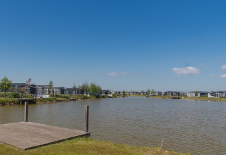 Udsigt over en sø med moderne hytter og en træbro på en solrig dag på et lodge-resort.