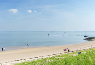 Familier nyder en solrig dag på en fredelig sandstrand med roligt vand og blå himmel ved lodgen.