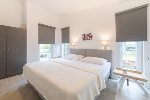 Lyst og moderne soveværelse med en stor seng, skab og vinduer med mørklægningsgardiner i Water Resort Oosterschelde 46.