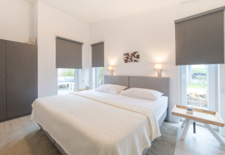 Lyst og moderne soveværelse med en stor seng, skab og vinduer med mørklægningsgardiner i Water Resort Oosterschelde 46.