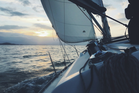 Sejlads ved solnedgang, set fra båddækket, med udsigt over havet og sejl mod en smuk horisont.