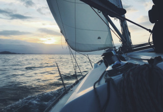Sejlads ved solnedgang, set fra båddækket, med udsigt over havet og sejl mod en smuk horisont.