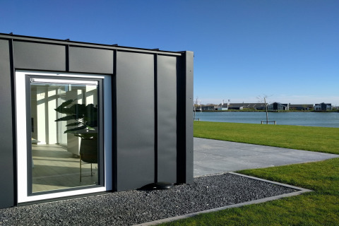 Moderne lodge ved Water Resort Oosterschelde 46 i Holland med udsigt over vand, grøn græsplæne og små huse.