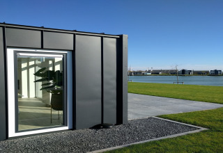 Moderne lodge ved Water Resort Oosterschelde 46 i Holland med udsigt over vand, grøn græsplæne og små huse.