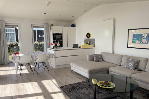 Moderne stue og køkken i Water Resort Oosterschelde 46 i Holland med sofa, spisebord og store vinduer.