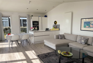 Moderne stue og køkken i Water Resort Oosterschelde 46 i Holland med sofa, spisebord og store vinduer.