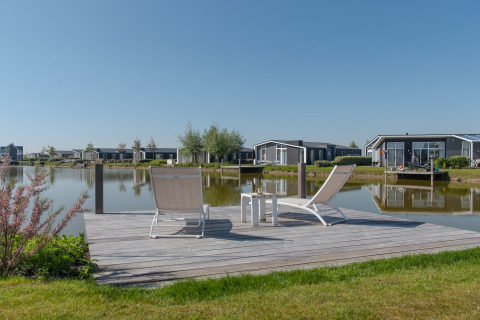 To liggestole på en træterrasse ved vandet på Water Resort Oosterschelde 46 i Holland, med moderne hytter.