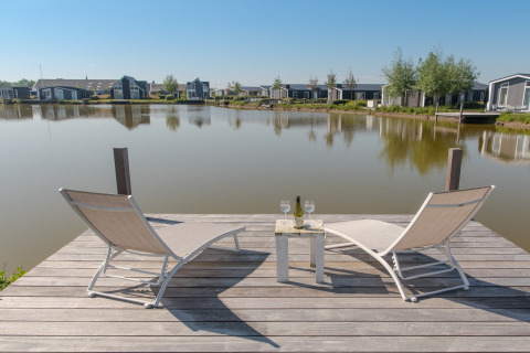 To liggestole på en træbro ved søen på Water Resort Oosterschelde 46, med udsigt over hytter i Holland.
