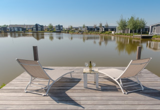 To liggestole på en træbro ved søen på Water Resort Oosterschelde 46, med udsigt over hytter i Holland.