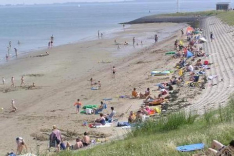 Persone che trascorrono una giornata di sole sulla spiaggia a gradoni, alcune nuotano e altre si rilassano.