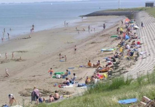 Persone che trascorrono una giornata di sole sulla spiaggia a gradoni, alcune nuotano e altre si rilassano.