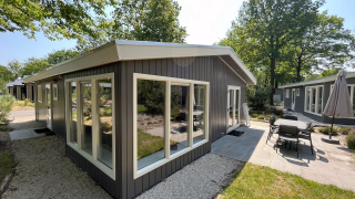 Modern Hackfort lodge with large windows and patio, surrounded by trees and greenery on a bright sunny day.