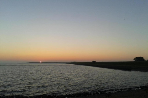 Solnedgang ved en lodge med udsigt over vandet, rolig himmel og silhuetter af landskab og træer.