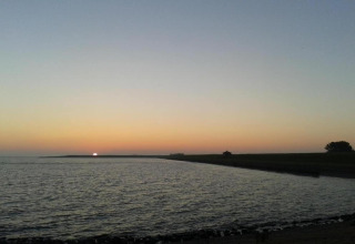 Solnedgang ved en lodge med udsigt over vandet, rolig himmel og silhuetter af landskab og træer.