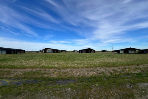 Udsigt over grønne marker og moderne hytter under en blå himmel ved Heerlijkheid Vlietenburg 1 i Holland.