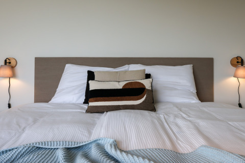 Indbydende seng med moderne puder og lamper på væggen, set på Heerlijkheid Vlietenburg 1-lodgen i Holland.