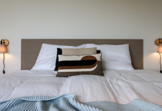 Indbydende seng med moderne puder og lamper på væggen, set på Heerlijkheid Vlietenburg 1-lodgen i Holland.
