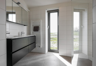 Moderne badeværelse i Heerlijkheid Vlietenburg 1 lodge i Holland, med store vinduer og sort møblement.