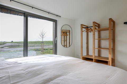 Moderne lodge soveværelse med stor seng, træskab og udsigt over grønne marker ved Vlietenburg, Holland.