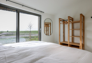 Moderne lodge soveværelse med stor seng, træskab og udsigt over grønne marker ved Vlietenburg, Holland.